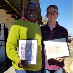 A students stands with a Zimbabwean man holding two certificates