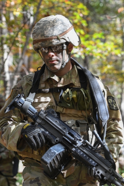 Cadet with rifle walks through the woods during Army ROTC training.
