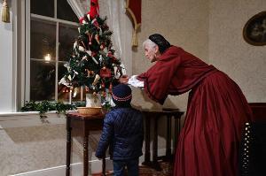 A guest interacts with an interpreter in period costume in front of a Christmas Tree at the Jackson House Museum.