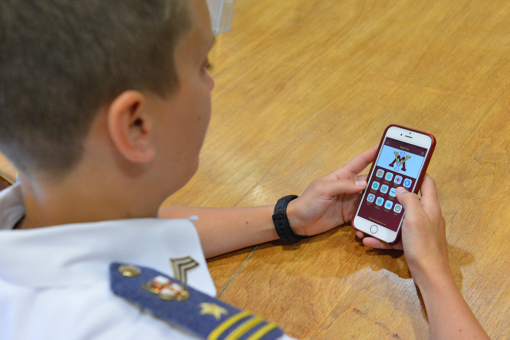 A cadet holds a cell phone displaying the Reach Out app.