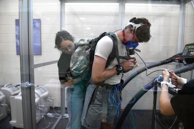 Abaigeal Doody ’23 adjusts 65-pound rucksack on the back of a male subject in the hypoxic chamber to test for stress at VMI. -VMI Photo by Marianne Hause.