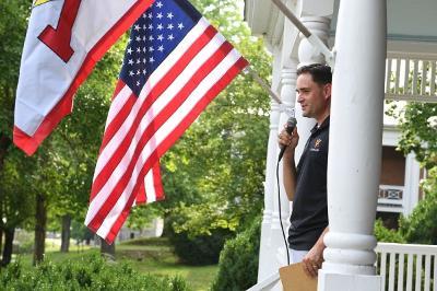VMI Chaplain John Casper '04 speaks while holding a microphone near an American flag.