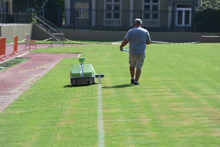 Willy Lilly walks beside Carl, as it paints lines on Alumni Memorial Field at Foster Stadium.