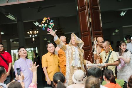 Kanokpon “Gun” Mettasat ’27 tosses treats and lucky coins to friends and family celebrating his time as a monk last June at Wat Khlong Khru Buddhist temple in Bangkok